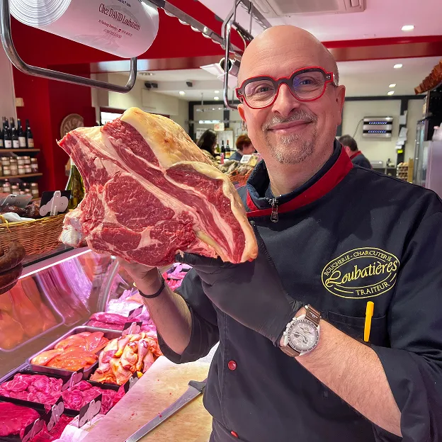 Boucher souriant présentant une grande pièce de bœuf cru dans son magasin à Toulouse en Haute-Garonne 31