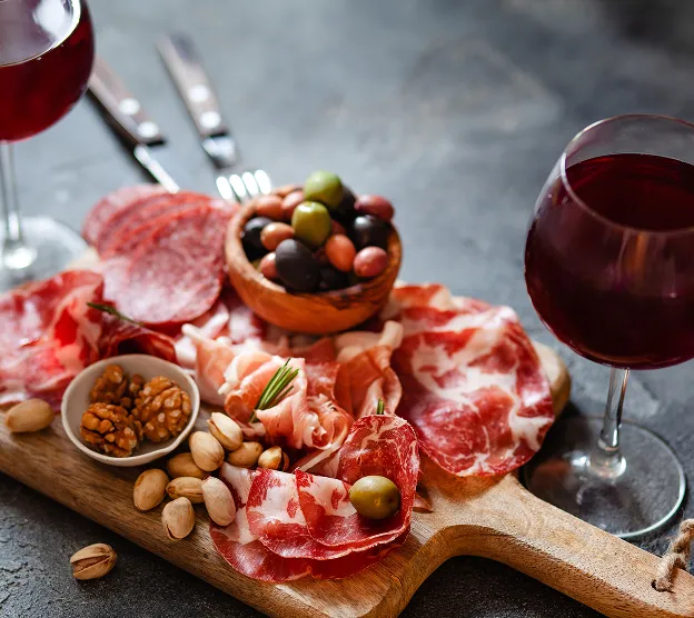Planche à charcuterie avec jambon, salami, olives, noix, pistaches et deux verres de vin rouge à Toulouse en Haute-Garonne 31