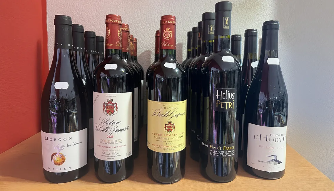 Une rangée de bouteilles de vin rouge avec des étiquettes variées sur une étagère en bois à Toulouse en Haute-Garonne 31